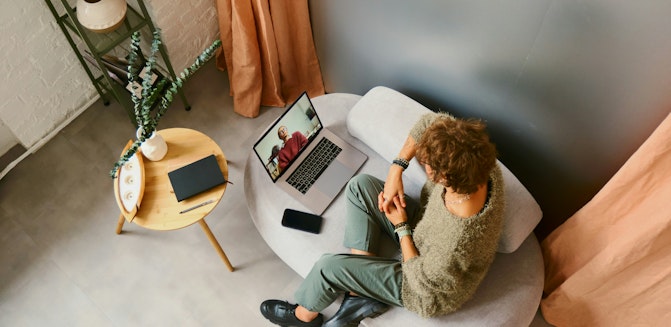 A person sitting on a couch with hands crossed, talking to their therapist on a video call about ending therapy.