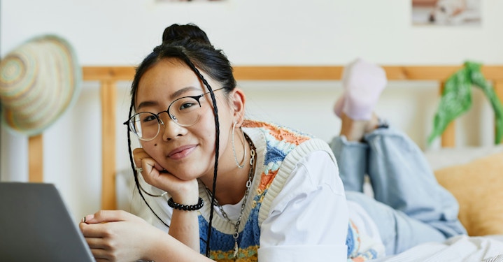 A teen lying comfortably on their bed with a laptop, smiling softly while exploring AI therapy online.