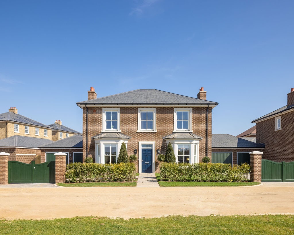 A georgian style detached home with brick facade, blue front door, bay windows and a double garage to the left hand side.