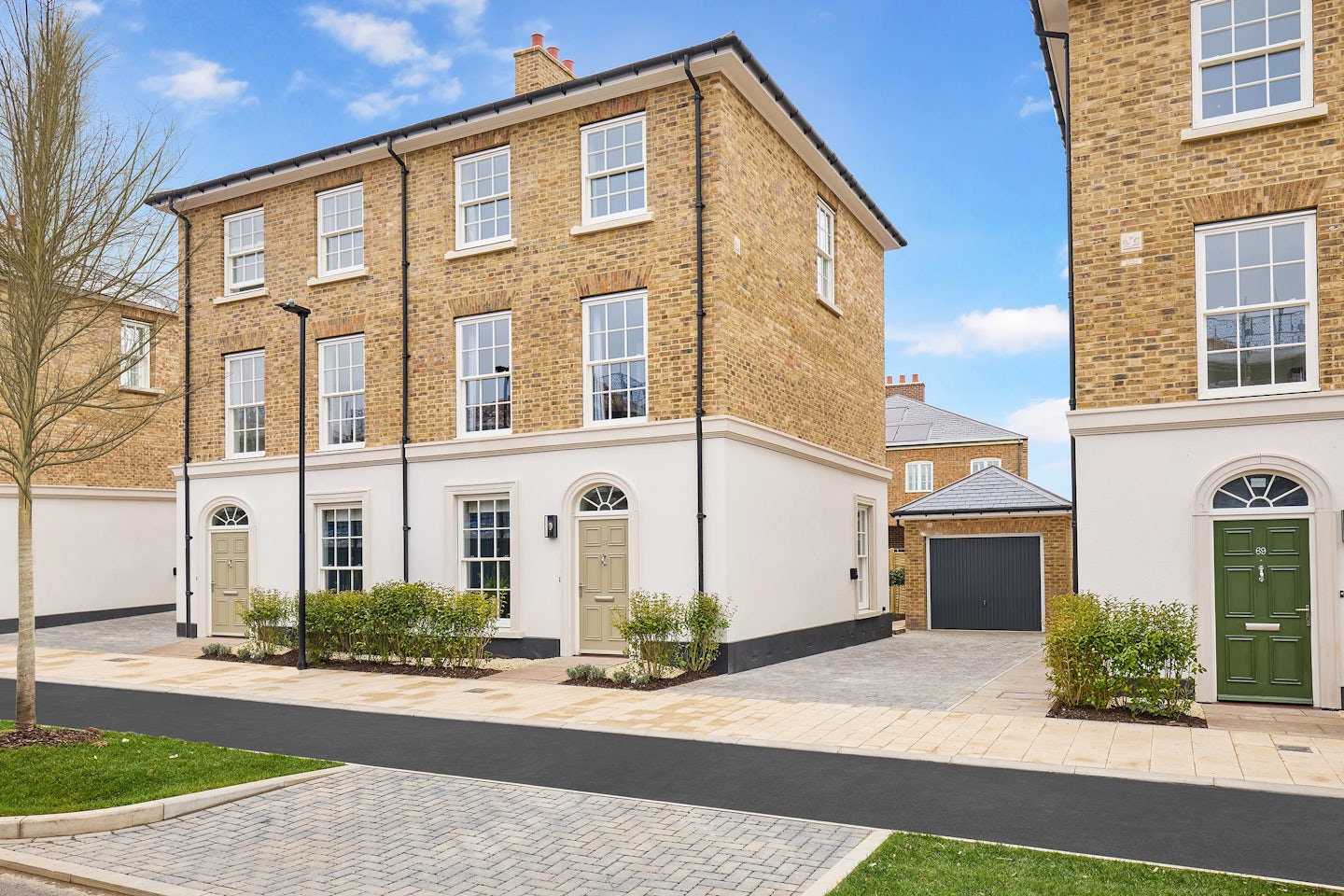 A row of modern Burlington townhouses with classic Georgian style brick exteriors and white accents at Welborne Garden Village. Each townhouse features large sash windows, a front door, and a small garden area with neatly trimmed shrubs. The paved driveway leads to a garage.