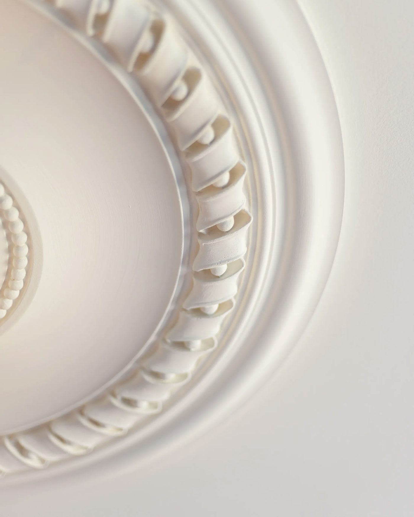 This image shows a decorative ceiling medallion with intricate designs. The medallion has curved, raised elements arranged in a circular pattern, with a small central detail. It highlights craftsmanship and adds elegance to a room.