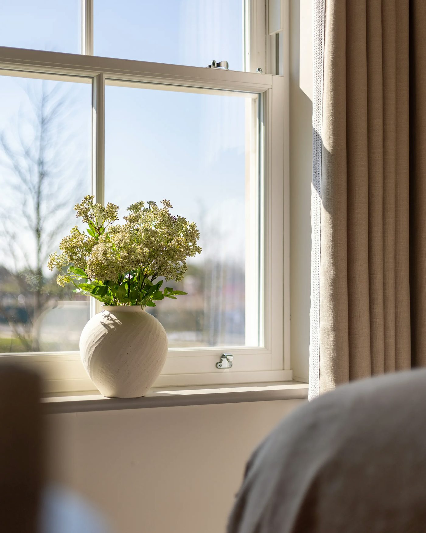 Sash window with a white vase holding a green plant with small white flowers on the windowsill.