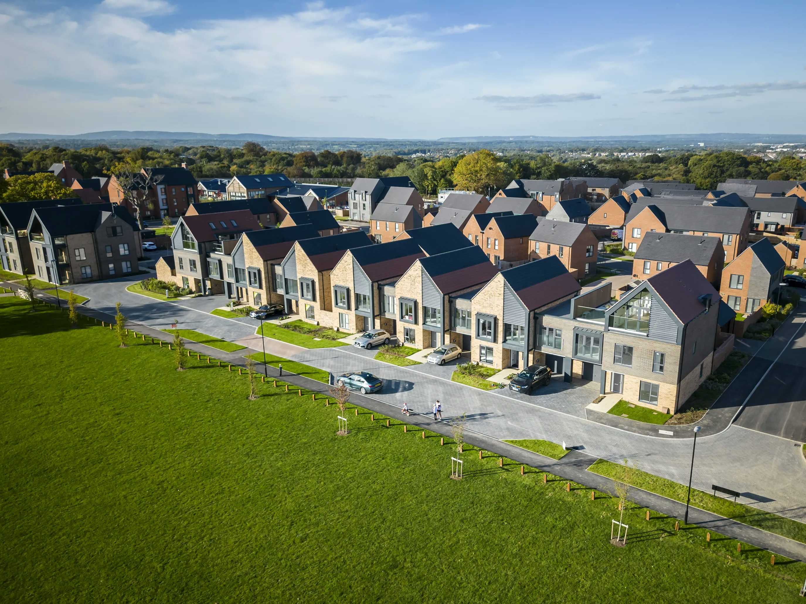 A row of nordic style villas on the village green with brick houses scattered behind at Woodgate at Pease Pottage.