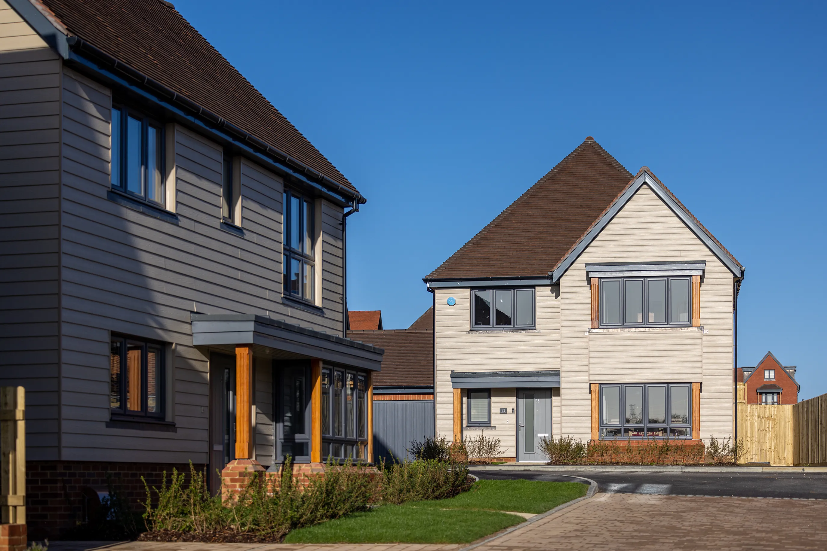 Two new build houses clad in light grey sit near each other.