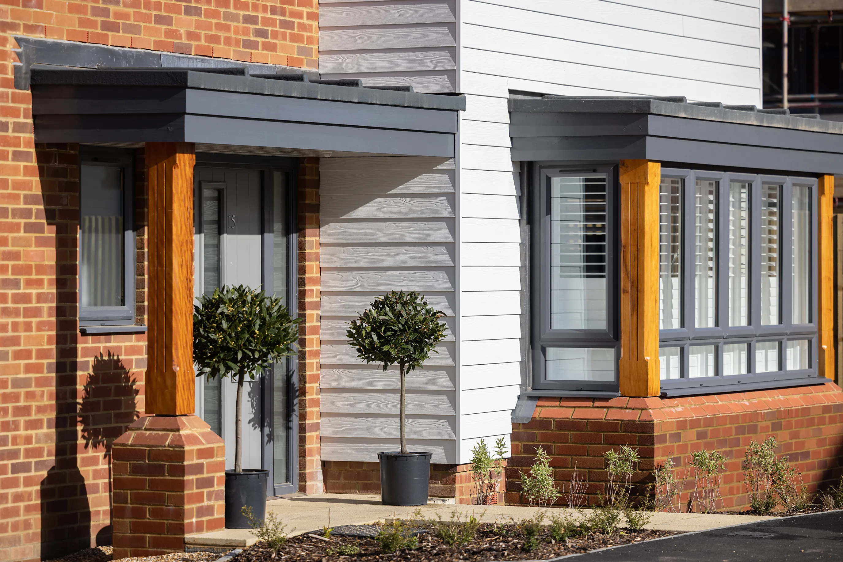 A close shot of a new home showing the front door which is bricked, and a large bay window which is flanked by light grey cladding.