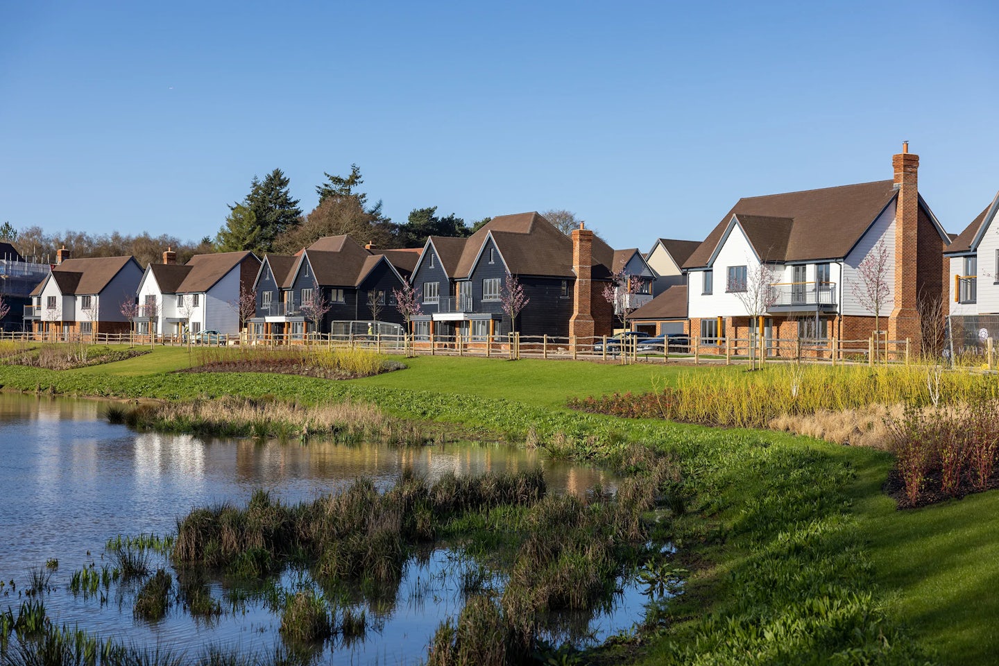 A row of large family homes along the side of a large lake. Houses are clad in black and white, with large double garages.