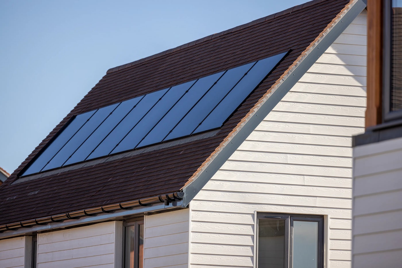 A row of solar panels are fitted into the roof of a new home clad in white composite cladding.