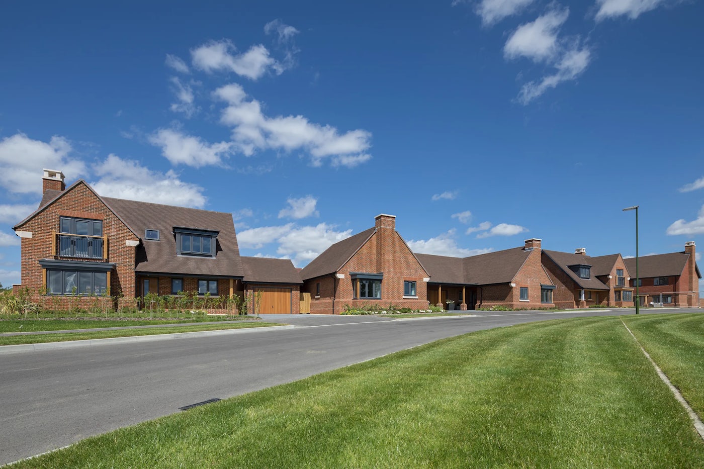 A row of bungalows and detached family homes sit on a wide road and in front of a large green space. Homes are brick.