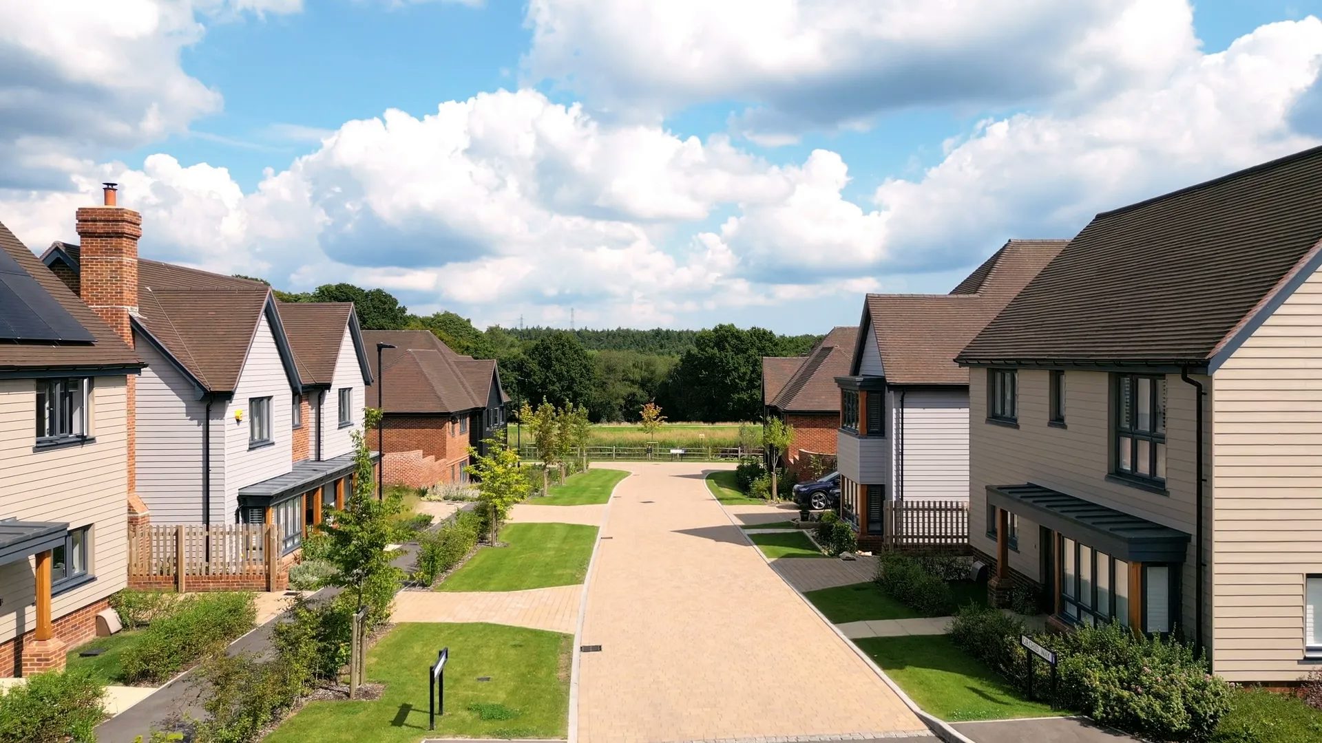 A street view towards the lake and forest at woodgate at Pease Pottage. Houses are clad in light grey and beige cladding.