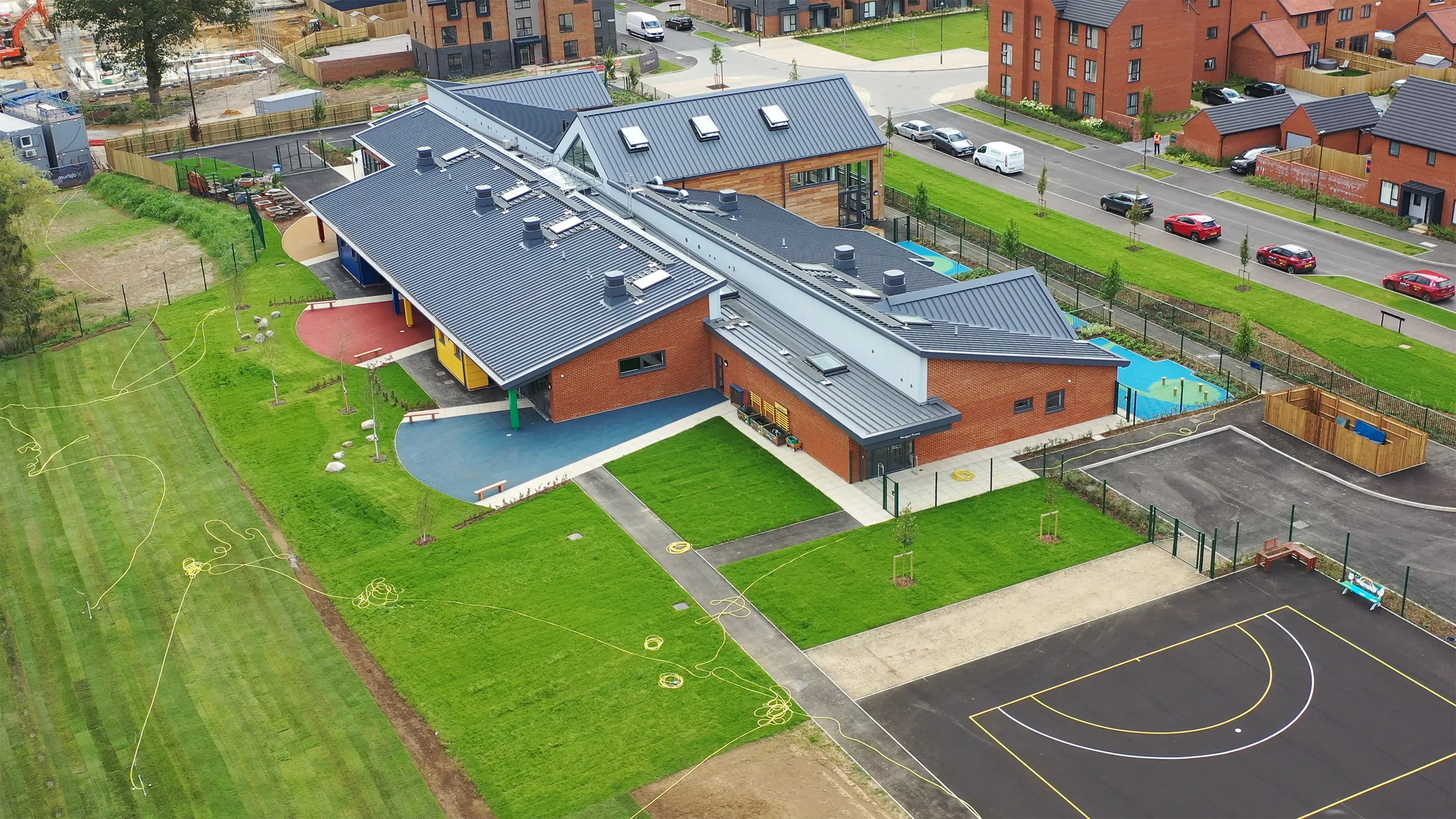 An aerial view of Woodgate Primary School. A play area, and sports courts can be seen.