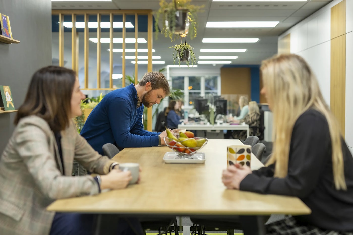 A group of office workers sit in a kitchen break out space and are engaged in conversation.
