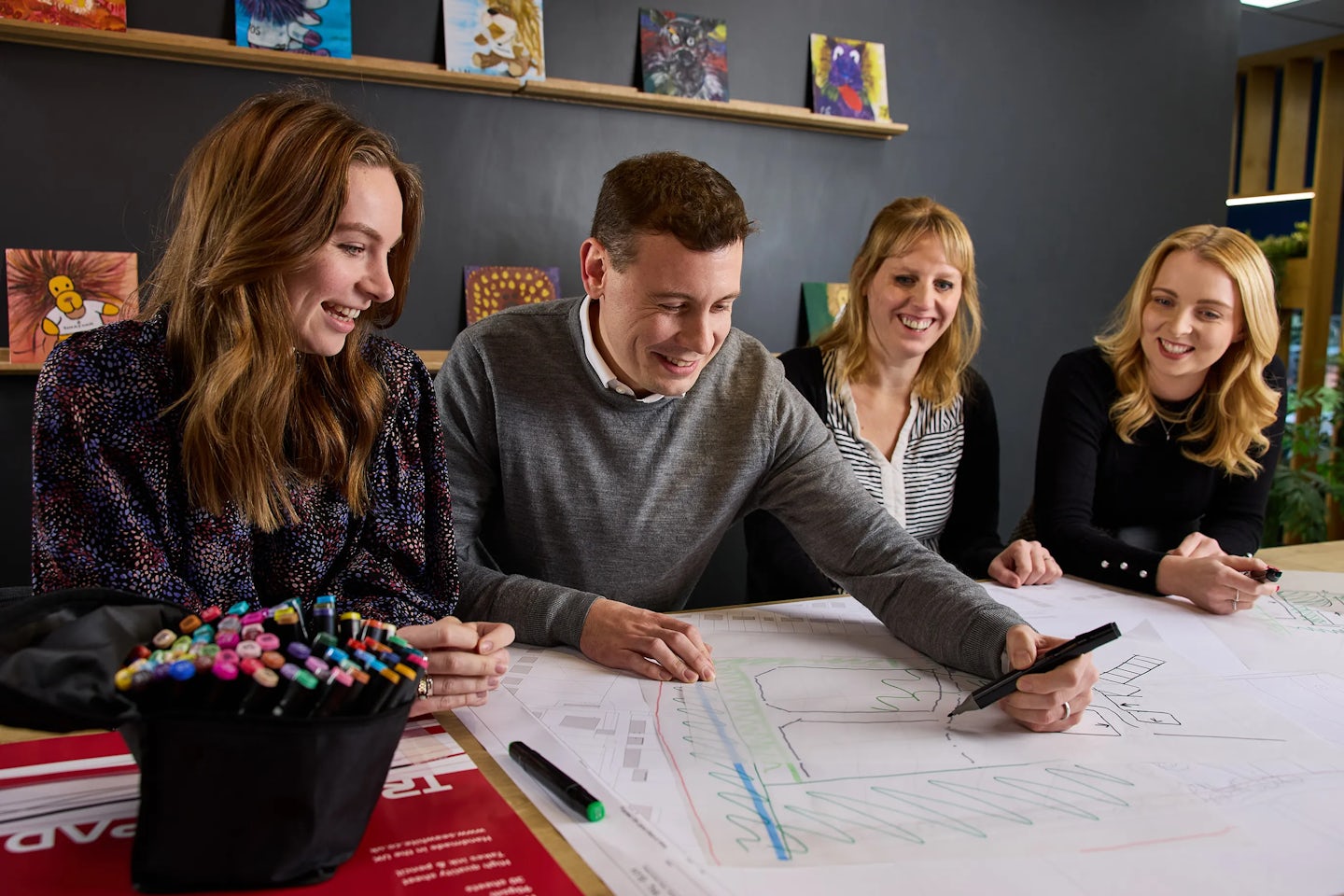 A group of four office workers sit around a table reviewing designs of houses.