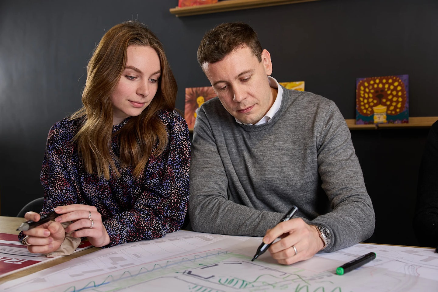 Colleague sit in an office location using marker pens to annotate a design of a house.