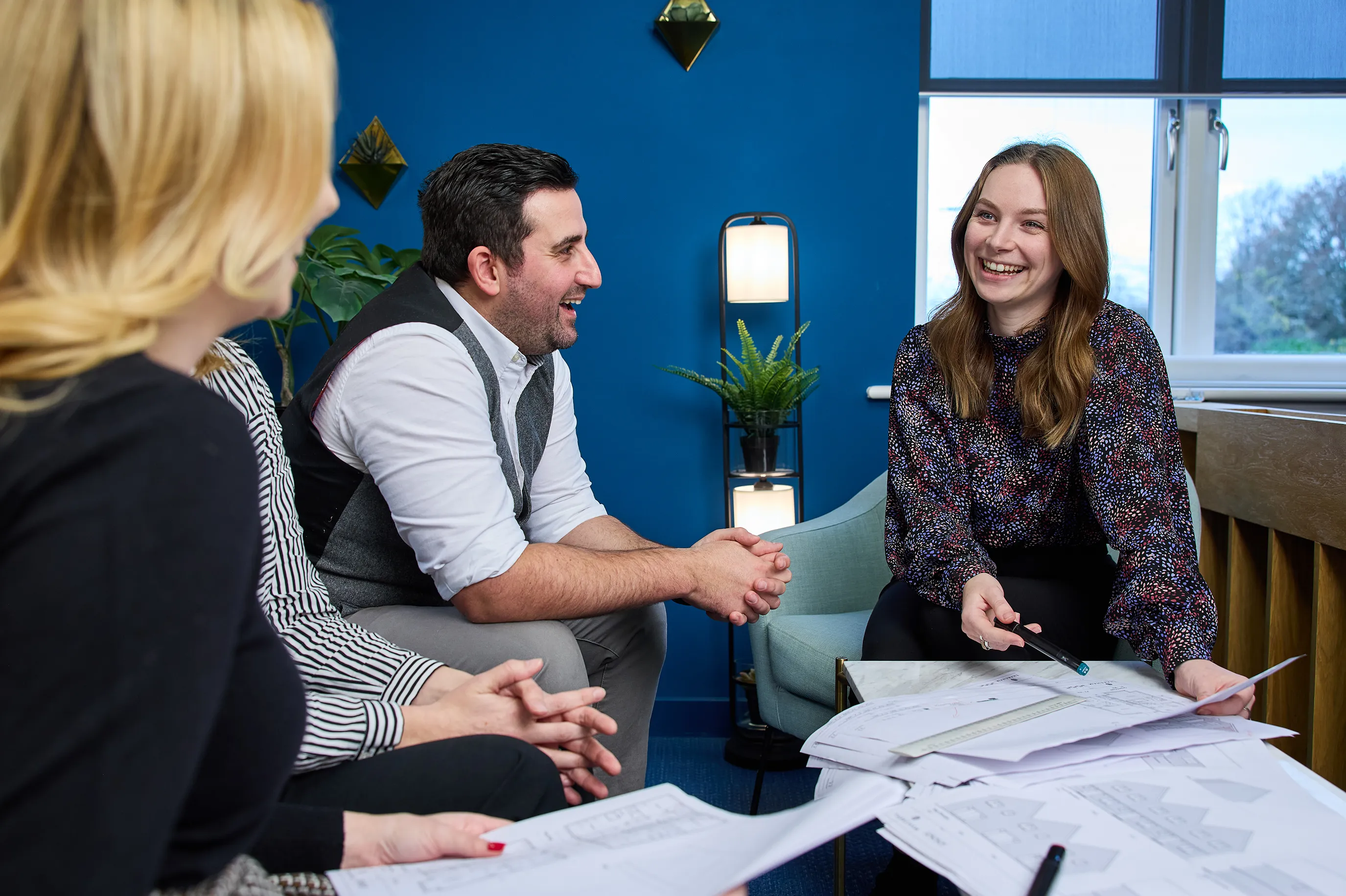 A group of four office workers sit around a low table reviewing designs of houses.