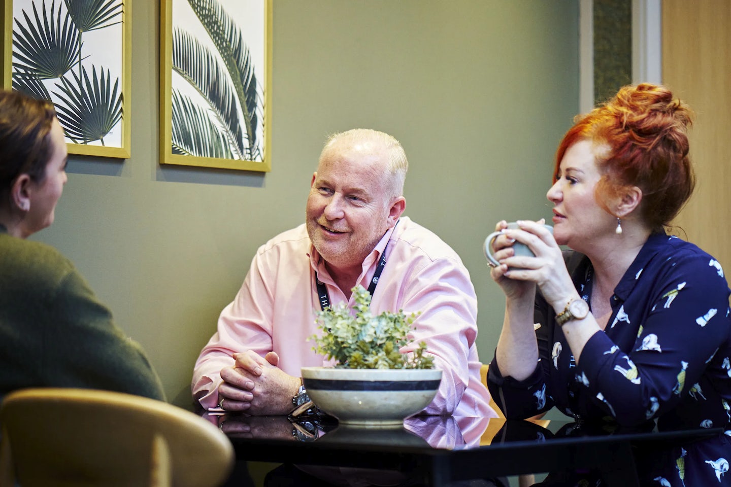 Three colleagues sit in conversation in an office break out space.