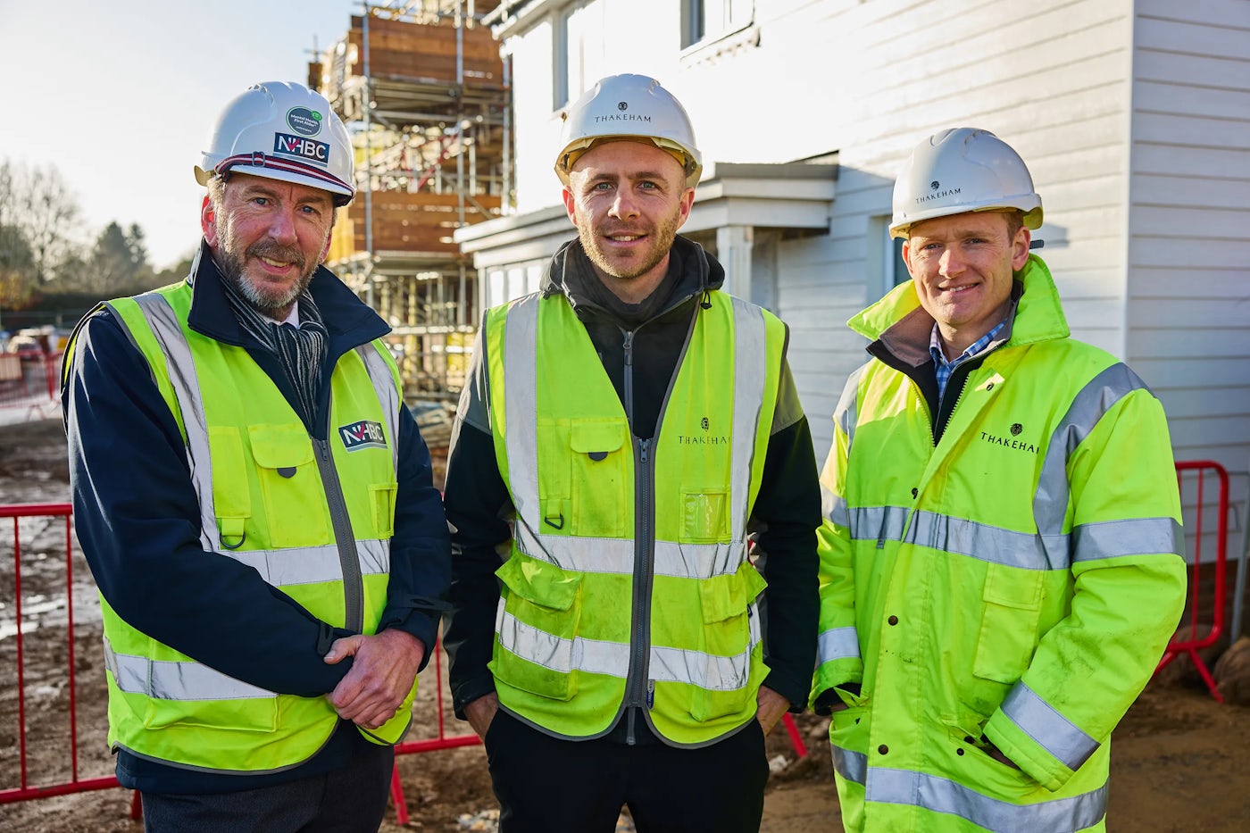 Three men in high vis jackets and hard hats pose of a photo in front of houses under construction.
