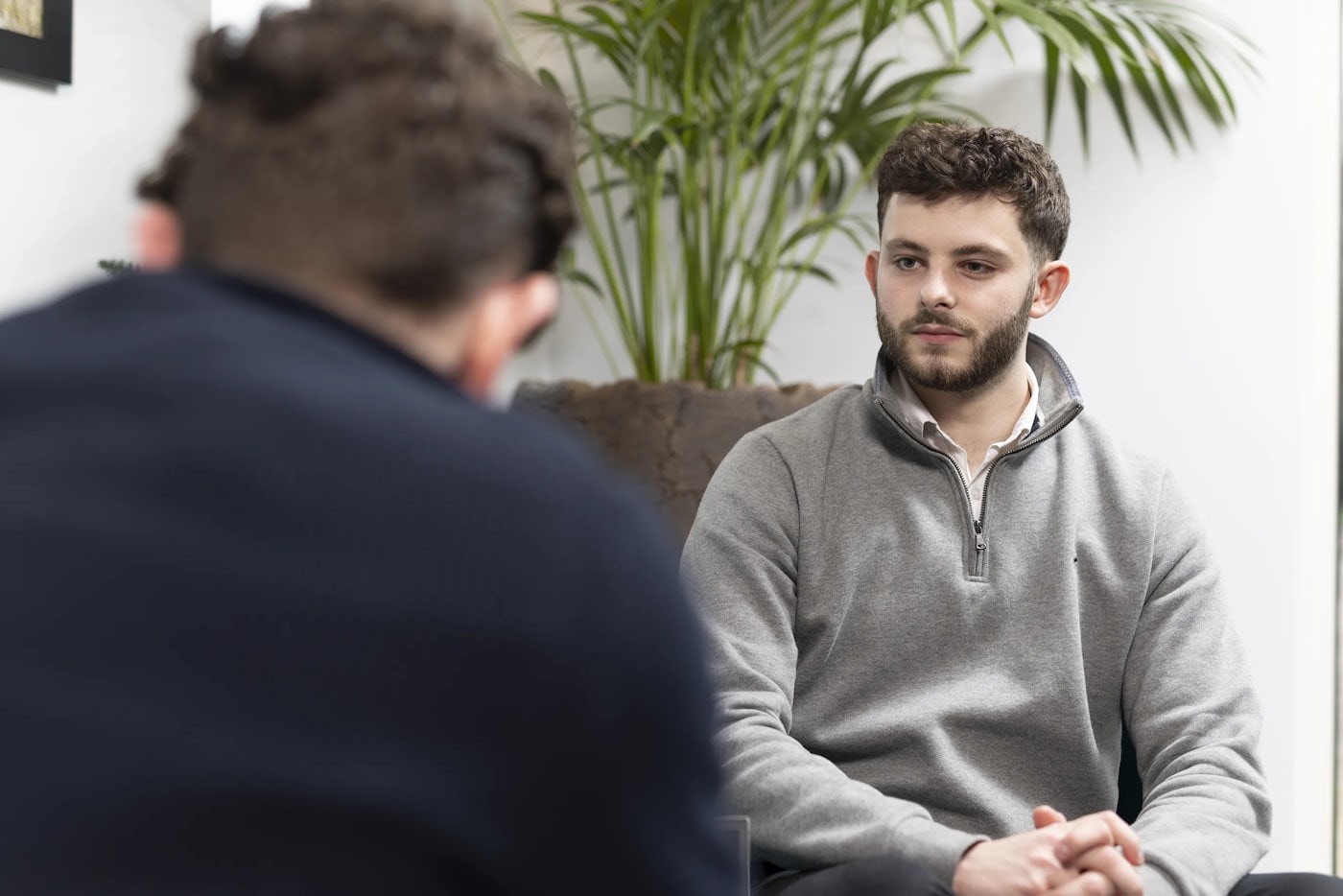 Colleagues sit in an office environment. one facing the camera and one facing away from the camera.
