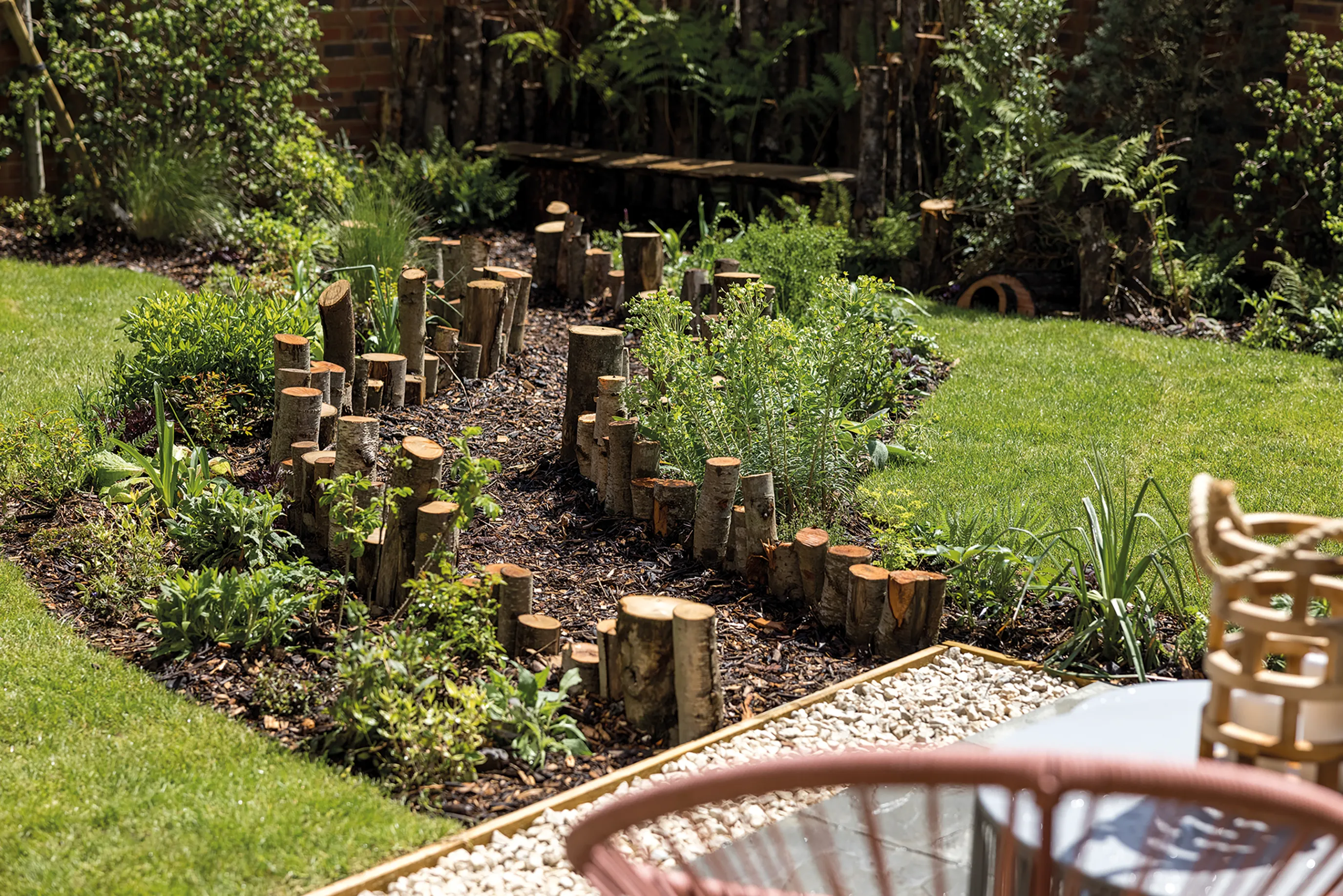 A garden path cuts through a lawn with wildlife friendly planting. Wooden trunks of different heights mark the pathway.