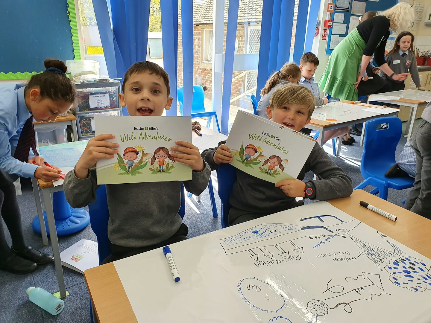 Two children in grey school uniforms hold copies of the eddie and ellies wild adventure book.