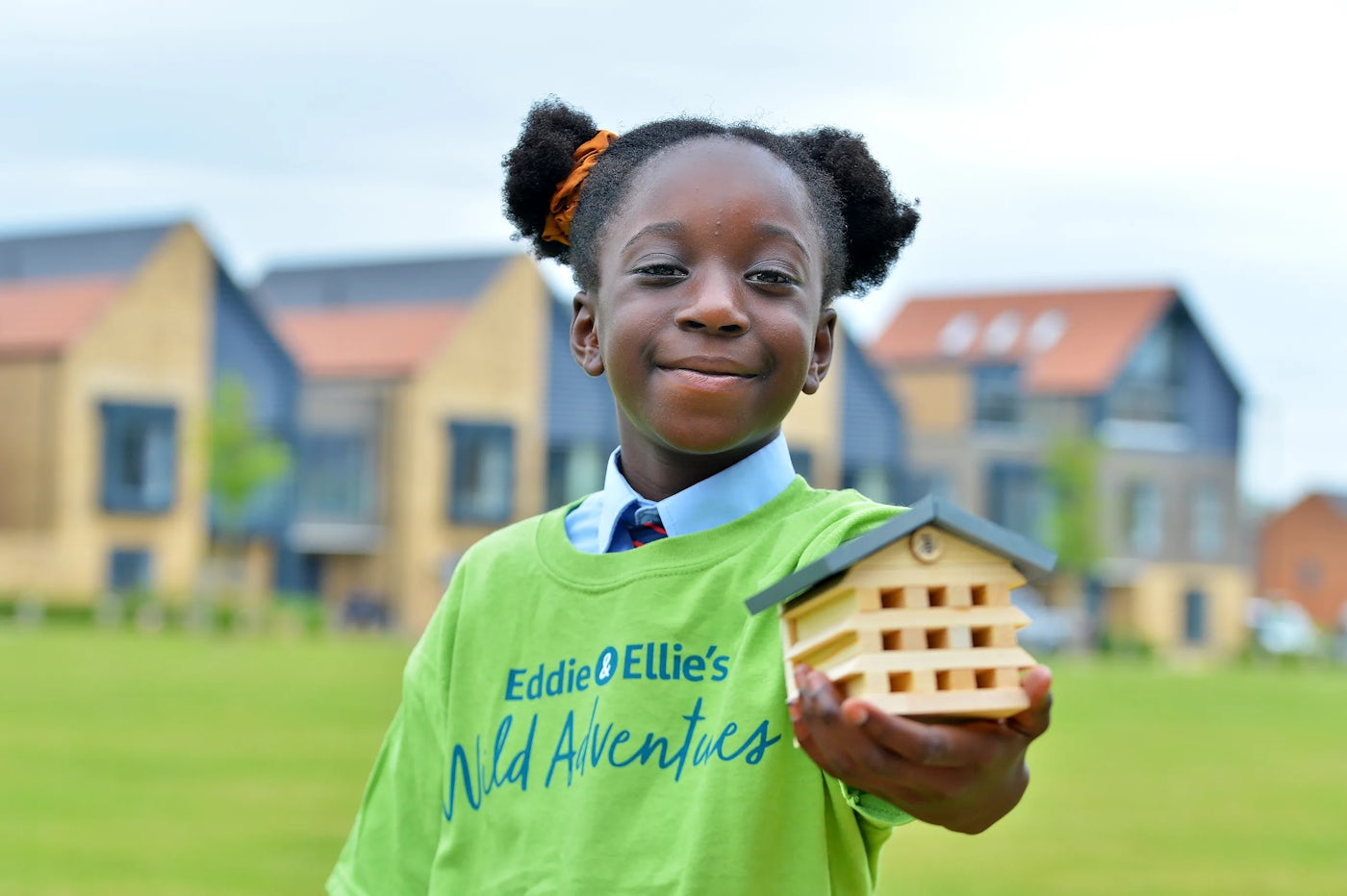 a child takes part in the eddie and ellie activity to create bee hotels. Out of focus behind them is a nordic style villa at Woodgate.