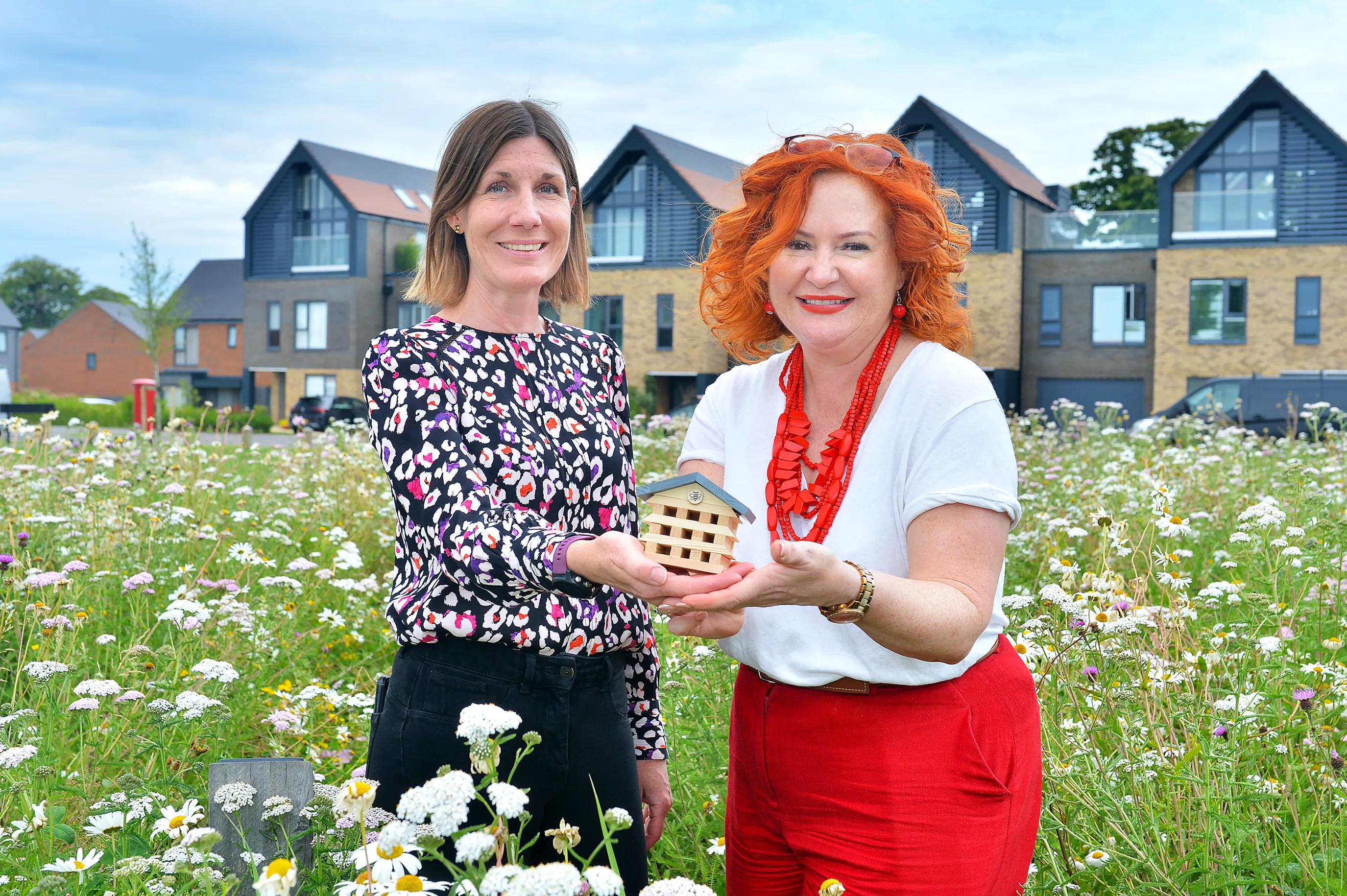 Sarah and Sam hold a completed bee hotel in the Woodgate Meadow Maze. Behind them are nordic style villas.