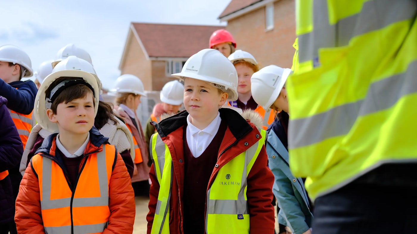 A group of children in high vis vests and hard hats visit a construction site.