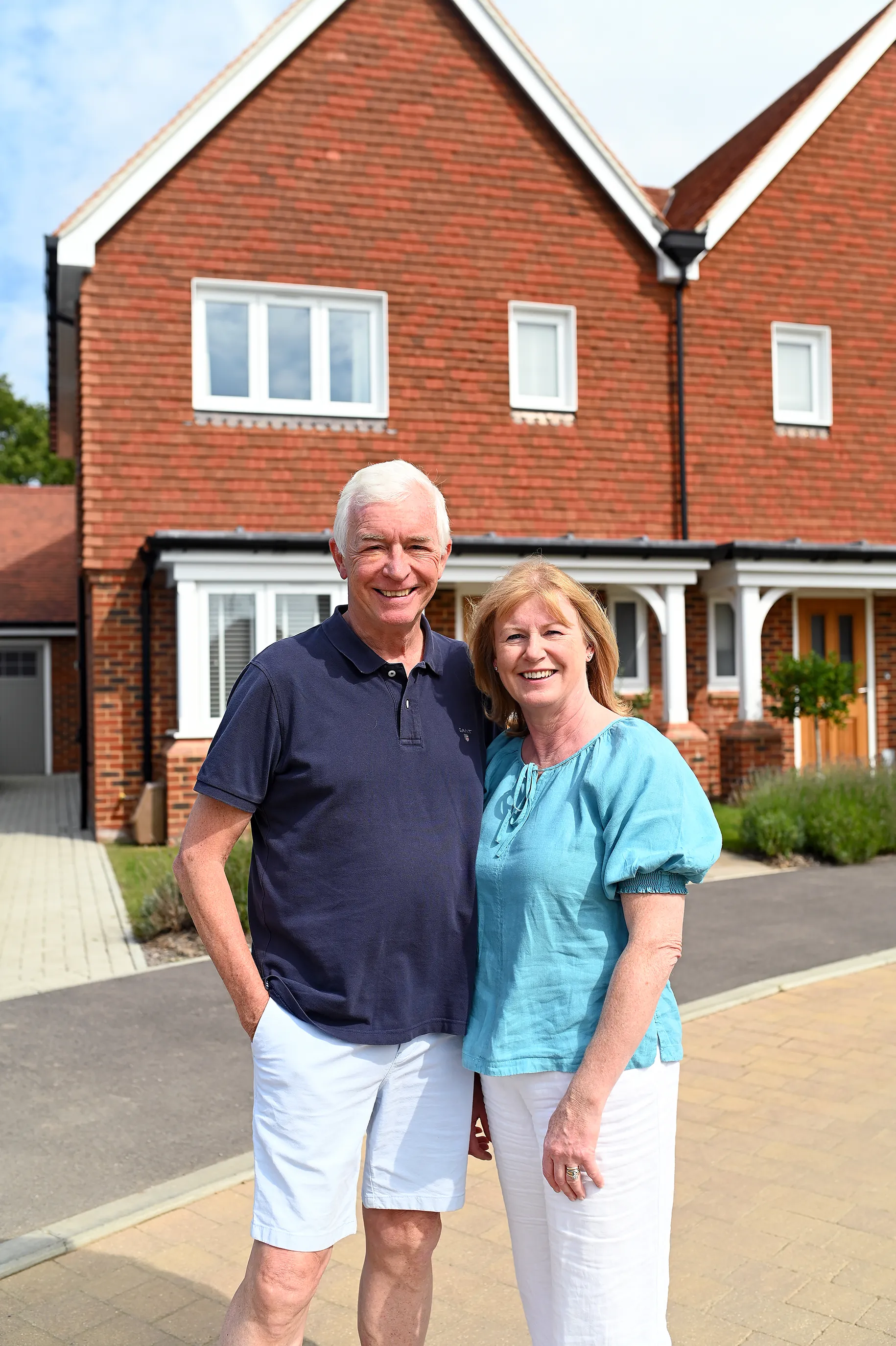 Jon and Sarah stand outside their new build home at Manorwood in Surrey. The brick semi detached new home is visible behind them, with a tile cladded upper floor.