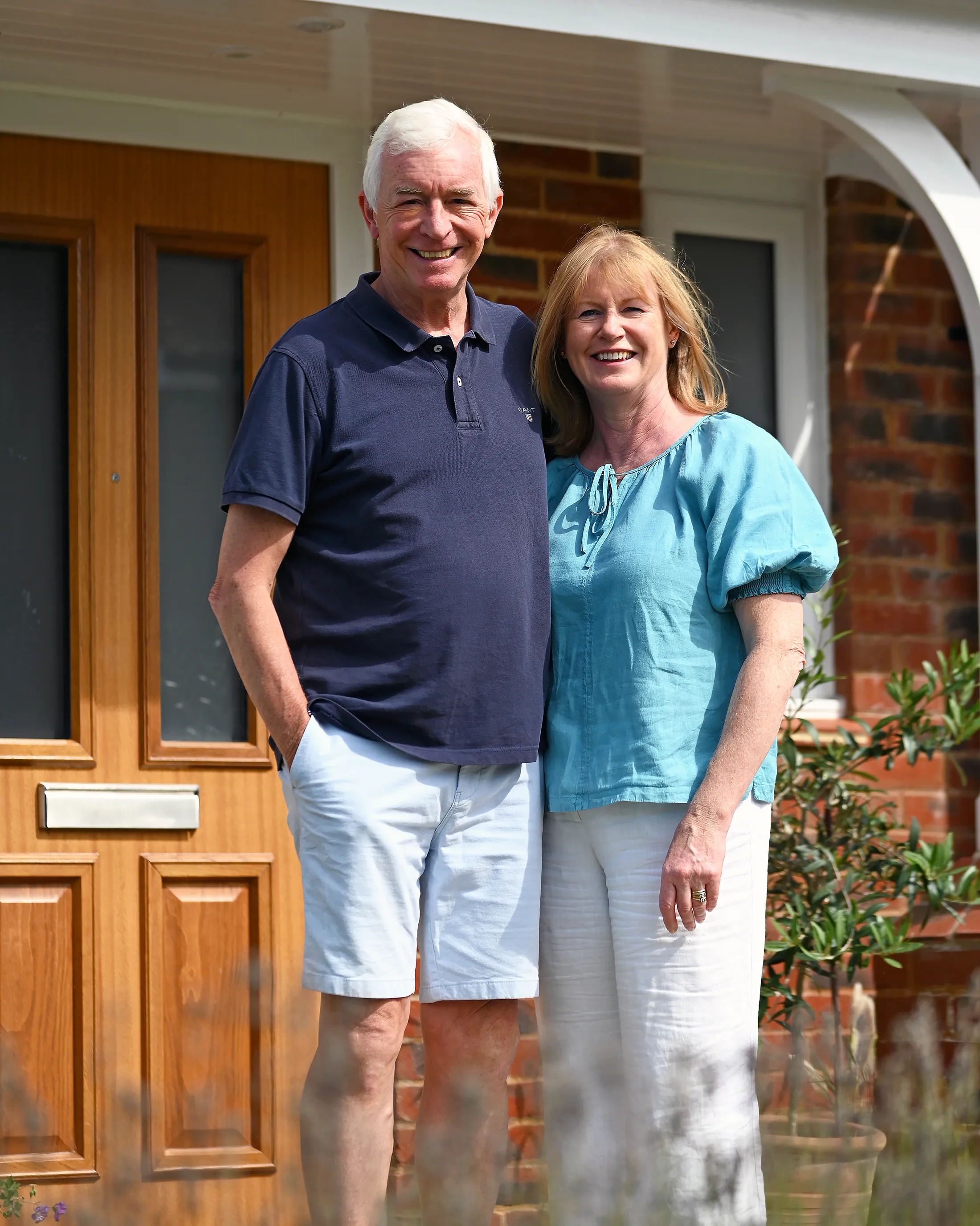 Jon and Sarah stand outside their new build home at Manorwood in Surrey. A light brown front door and bricks are visible behind thm.