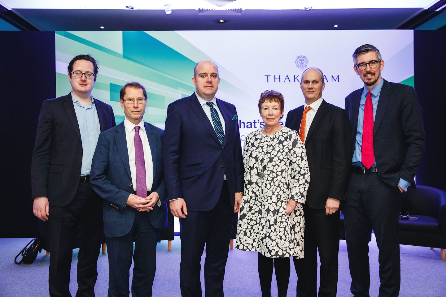 Six individuals stand together in business attire at a formal event.