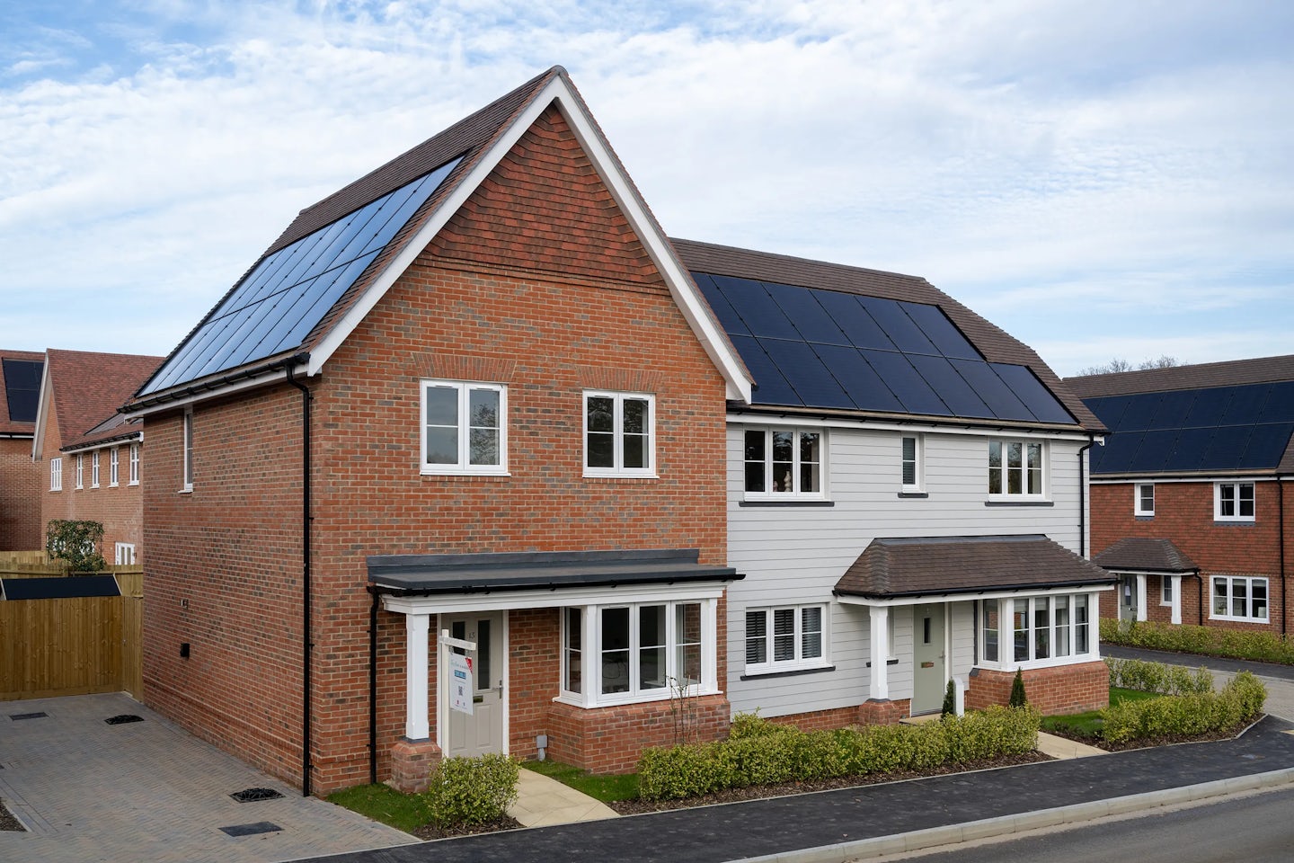 A modern suburban home with a pitched roof fitted with solar panels. The exterior combines brick and white siding, with multiple windows enhancing natural light. A neatly landscaped front garden adds to the welcoming aesthetic. The presence of solar panels suggests a focus on renewable energy and sustainability.