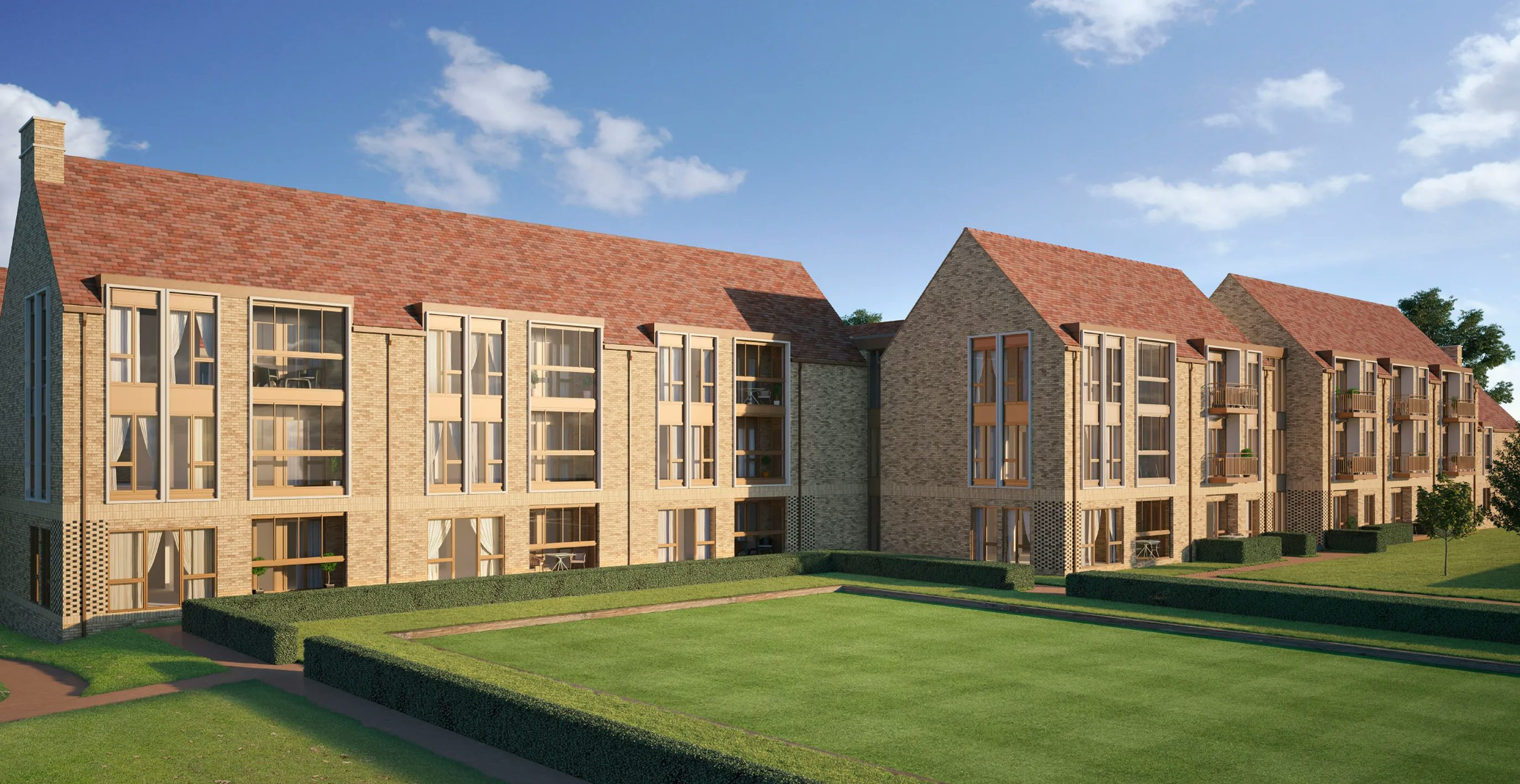 CGI of a modern residential complex featuring beige brick buildings with red-tiled roofs and large windows. The buildings are arranged in a uniform style around neatly trimmed green lawns and hedges. The clear sky with sparse clouds suggests a calm, sunny day.