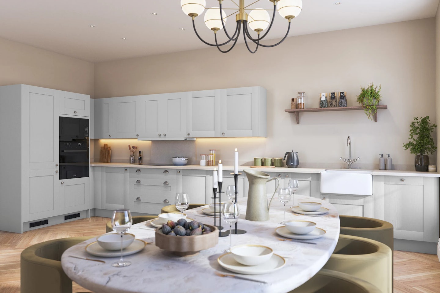 A contemporary kitchen and dining area with soft grey cabinetry, a white apron-front sink beneath an open wooden shelf adorned with jars and greenery, and a built-in oven. The foreground features a marble-topped dining table elegantly set with glassware, ceramic dishes, and a decorative bowl, beneath a sculptural multi-light chandelier that adds a warm, inviting glow. The space conveys a refined, modern aesthetic with a hint of rustic charm.