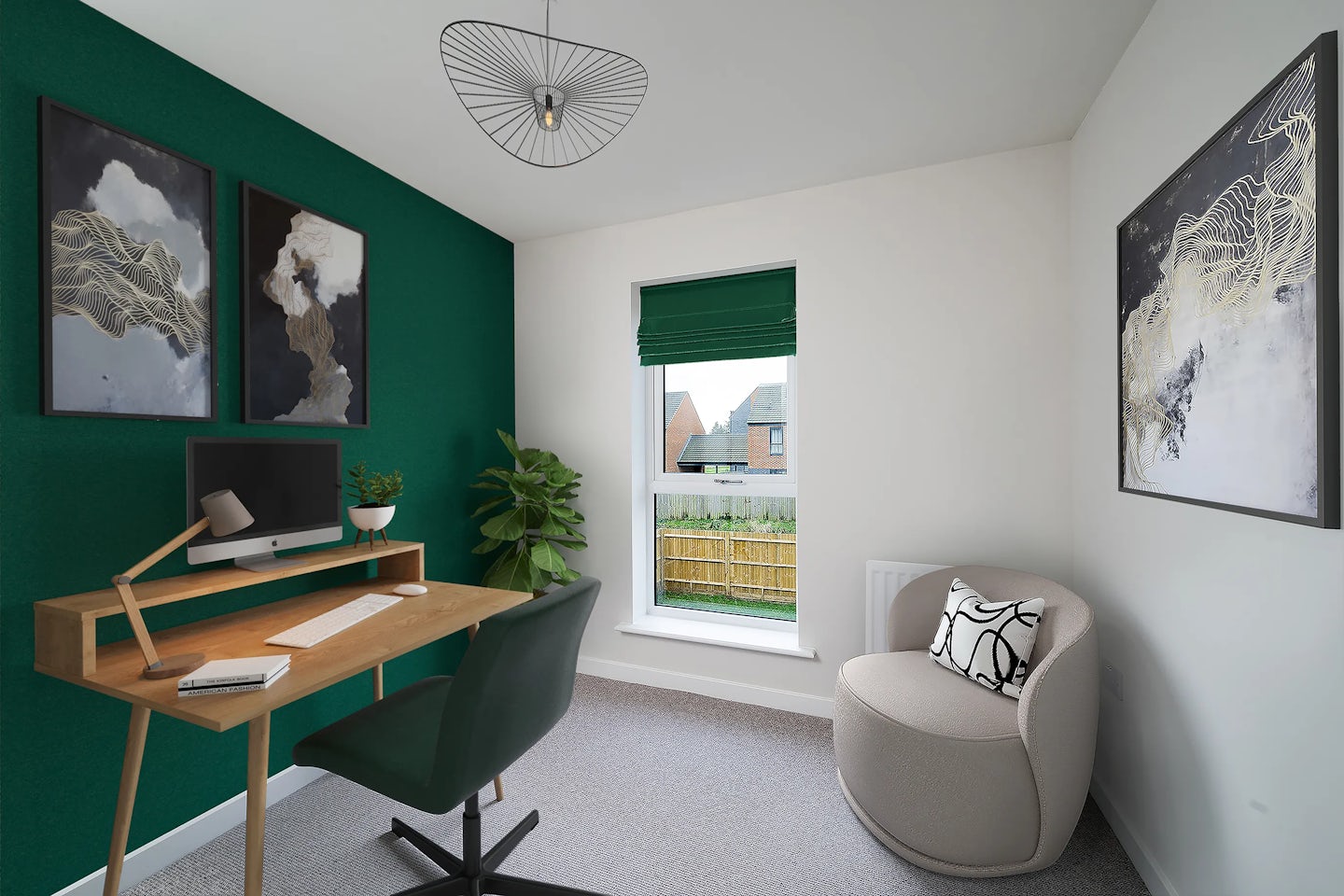 A modern home office with a warm, minimalist aesthetic. A wooden desk with a monitor, keyboard, mouse, notebook, and small potted plant faces a green feature wall adorned with two abstract framed artworks. A green swivel chair sits neatly at the desk. To the right, a beige armchair with a patterned cushion rests beside a window dressed in a green blind, offering a glimpse of a neighbouring house and wooden fence outside. Above the armchair hangs another abstract print. A sculptural wireframe light fixture hangs from the ceiling, and the light grey carpet adds softness to the space.