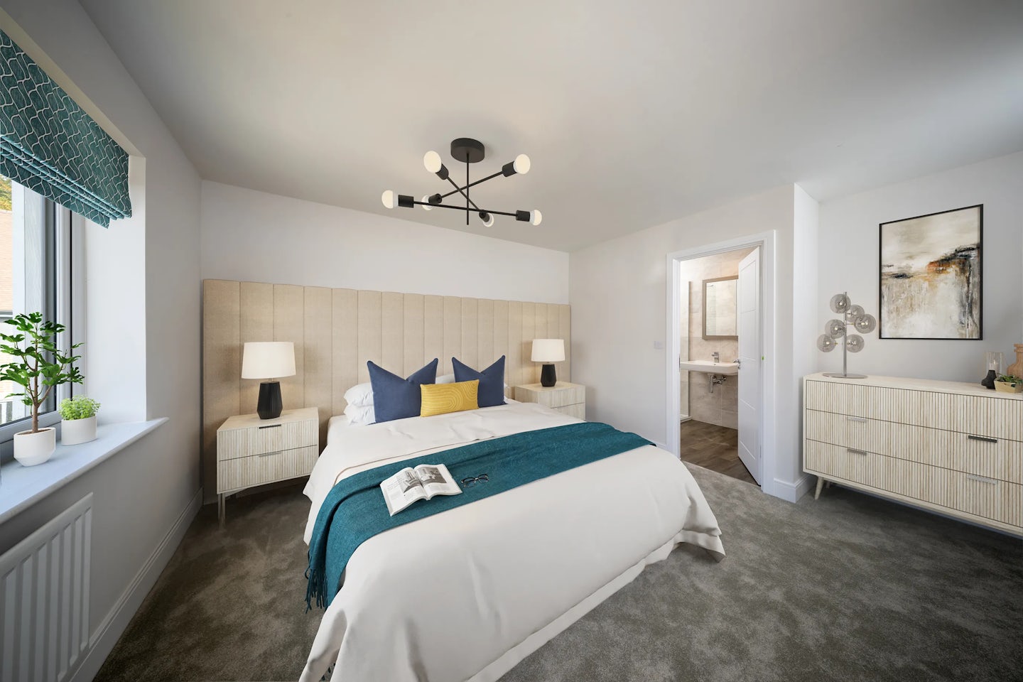A modern bedroom featuring a neatly made bed with white bedding, a teal throw, and accent pillows in dark blue and yellow. A book rests on the bed. The room includes matching nightstands with lamps, a contemporary chandelier overhead, and a window dressed with a patterned teal curtain and potted plants. To the right, a doorway leads to a bathroom, beside a dresser topped with a decorative lamp and framed abstract artwork. The space reflects a clean, minimalist design in neutral tones with modern furnishings.