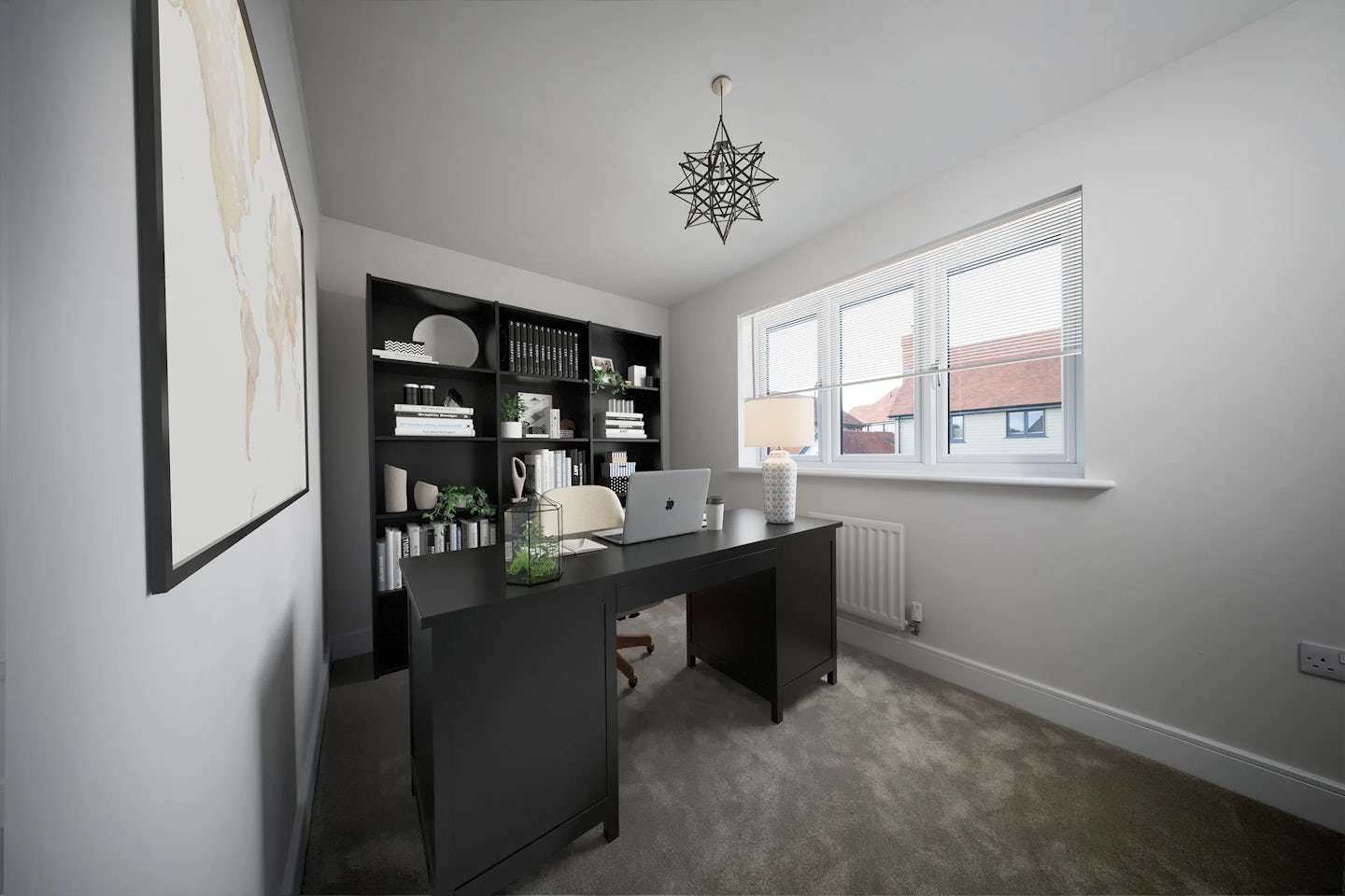 Modern home office with minimalist décor. A large black desk holds a laptop, desk lamp, and small decorative items. Behind it, a black shelving unit displays books, plants, and ornaments. Natural light streams through a window on the right. A star-shaped pendant light hangs from the ceiling, and a framed world map adorns the white wall to the left. The carpeted floor adds a soft contrast to the clean, monochromatic palette.