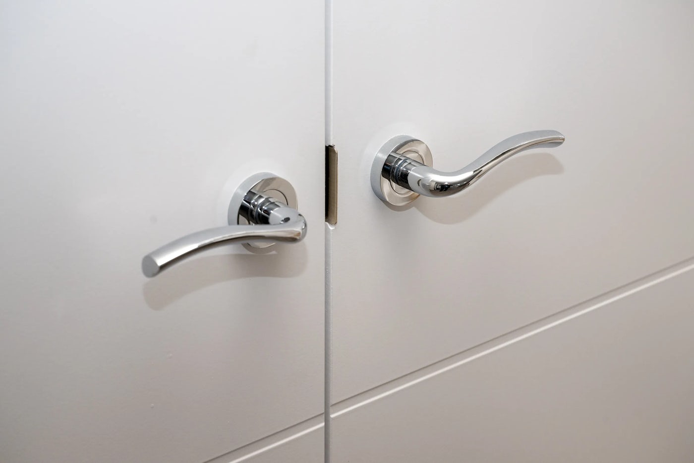 Close-up of two modern metallic door handles mounted symmetrically on a white double door, with a small circular feature at the point where the doors meet
