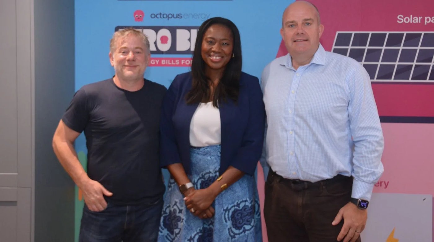 Three people standing in front of a promotional backdrop featuring the Octopus Energy logo and the slogan 'ZERO BILLS Energy Bills for Life,' with solar panel and battery storage graphics—highlighting a clean energy initiative focused on long-term affordability and renewable solutions.