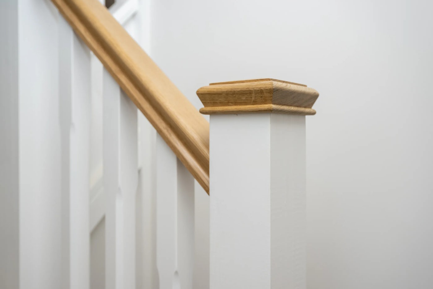 Close-up of a staircase newel post made of white-painted wood with a light brown wooden handrail.