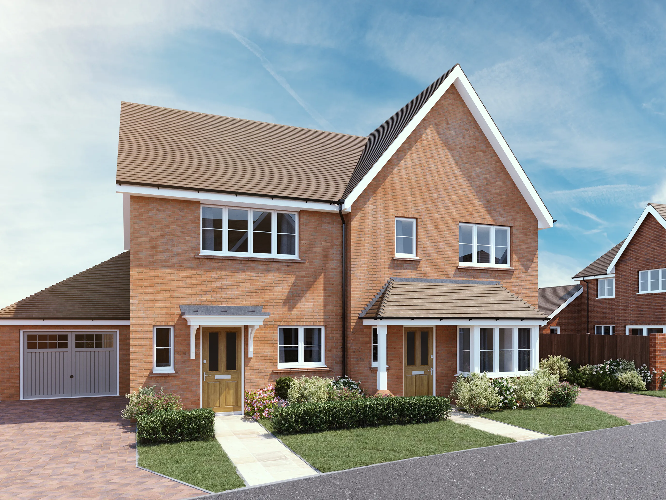 CGI of a modern semi-detached residential building composed of two red brick houses with pitched brown tile roofs and white-framed windows. Each home features its own entrance with a wooden front door and a small porch—one with white columns, the other with a larger canopy. The left house includes an integrated garage with a white door, while both properties are set within neatly landscaped front gardens with paved paths, trimmed grass, and blooming flowers. In the background, similar homes are visible beneath a clear sky with wispy clouds, adding to the calm, suburban setting