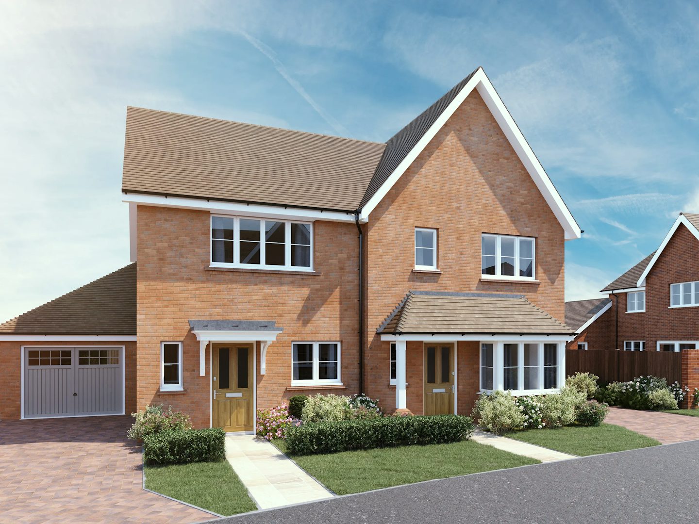 CGI of a modern semi-detached residential building composed of two red brick houses with pitched brown tile roofs and white-framed windows. Each home features its own entrance with a wooden front door and a small porch—one with white columns, the other with a larger canopy. The left house includes an integrated garage with a white door, while both properties are set within neatly landscaped front gardens with paved paths, trimmed grass, and blooming flowers. In the background, similar homes are visible beneath a clear sky with wispy clouds, adding to the calm, suburban setting