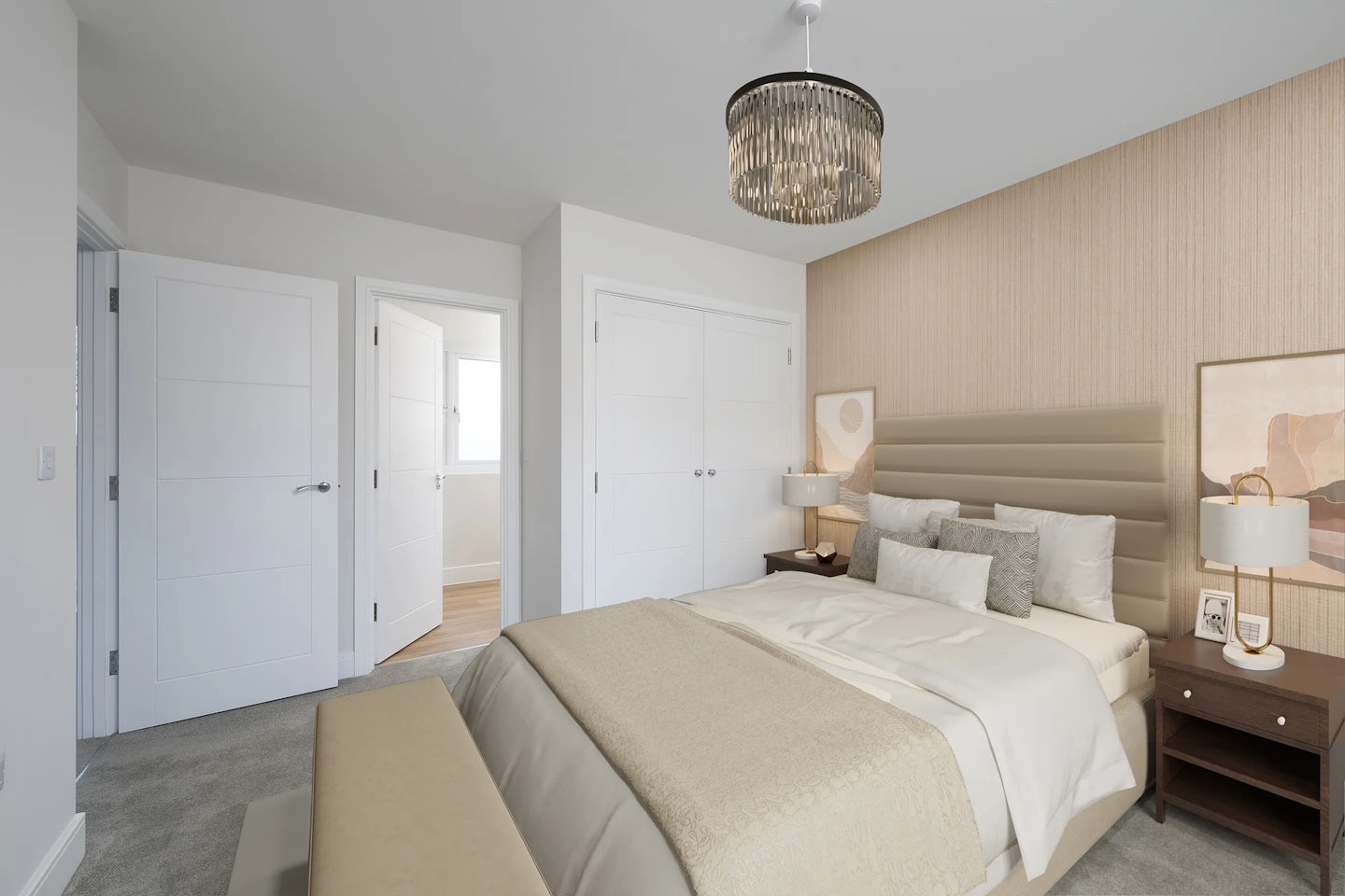 Well-appointed bedroom featuring a large double bed with a padded beige headboard, layered cream and taupe bedding, and an assortment of decorative pillows. Matching nightstands flank the bed, each topped with a sleek lamp and elegant ornaments. A soft carpet covers the floor, and a cushioned bench sits at the foot of the bed. The wall behind the bed is adorned with textured wallpaper in a light neutral tone, and a chandelier adds ambient refinement above. Visible in the background are two doors—one double-doored closet and one open doorway leading to an adjoining room filled with daylight, completing the serene and stylish atmosphere