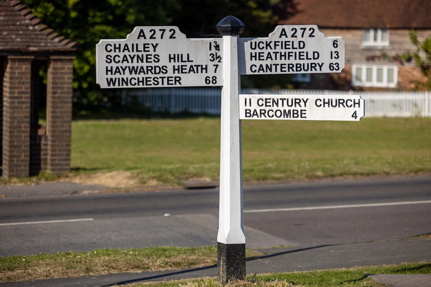 White roadside signpost with black text and four directional arms showing distances to locations including Chailey, Scaynes Hill, Haywards Heath, Winchester, Uckfield, Heathfield, Canterbury, and a 2nd-century church in Barcombe.