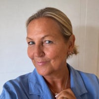 Michelle wears a blue shirt and stands in front of a white wall. She has blond hair tied back.