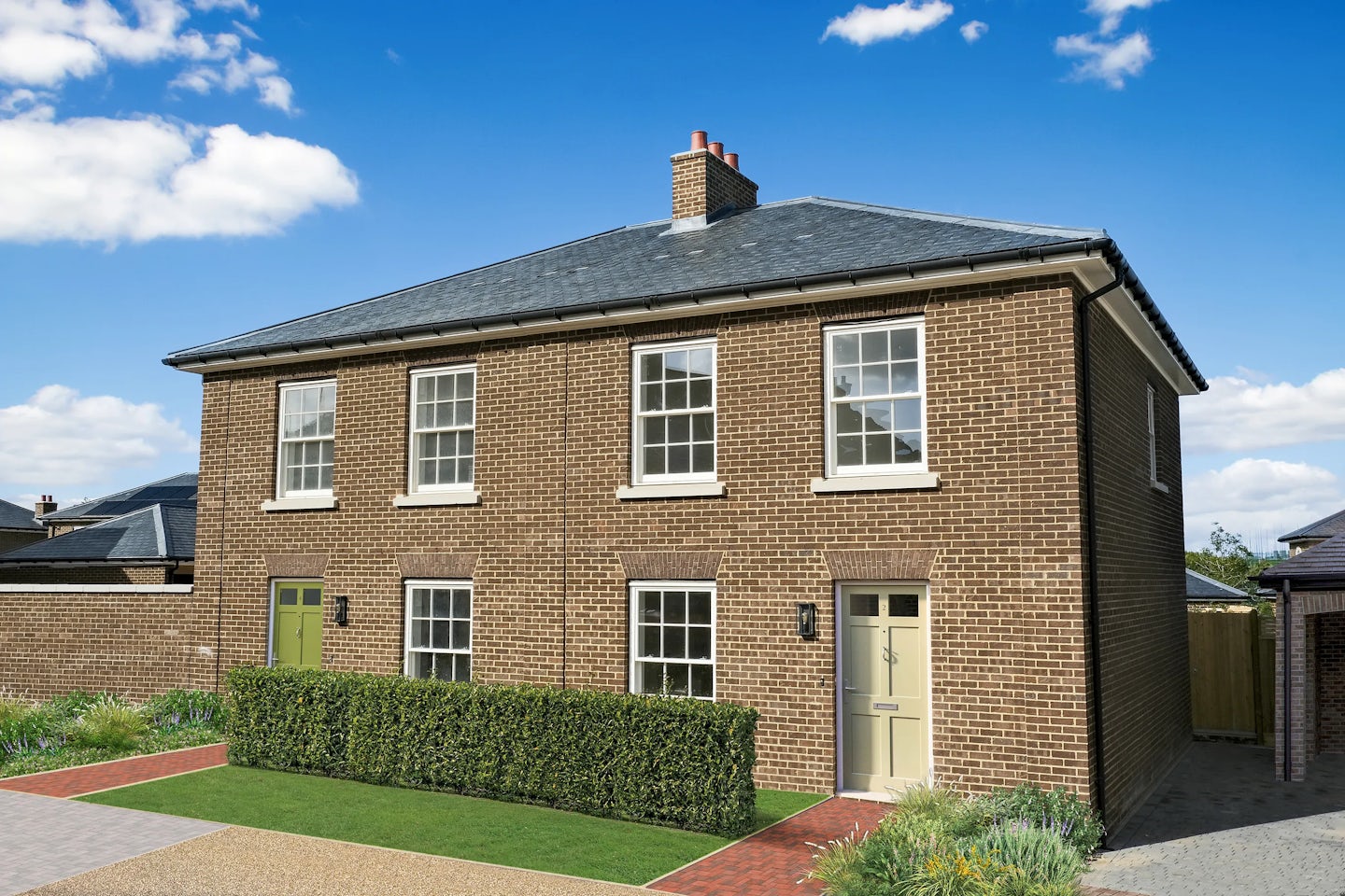 A semi-detached brick house with symmetrical design, featuring two entrances—one with a green door and the other with a beige door—four upper windows, and a hedge-lined front lawn under a partly cloudy sky.