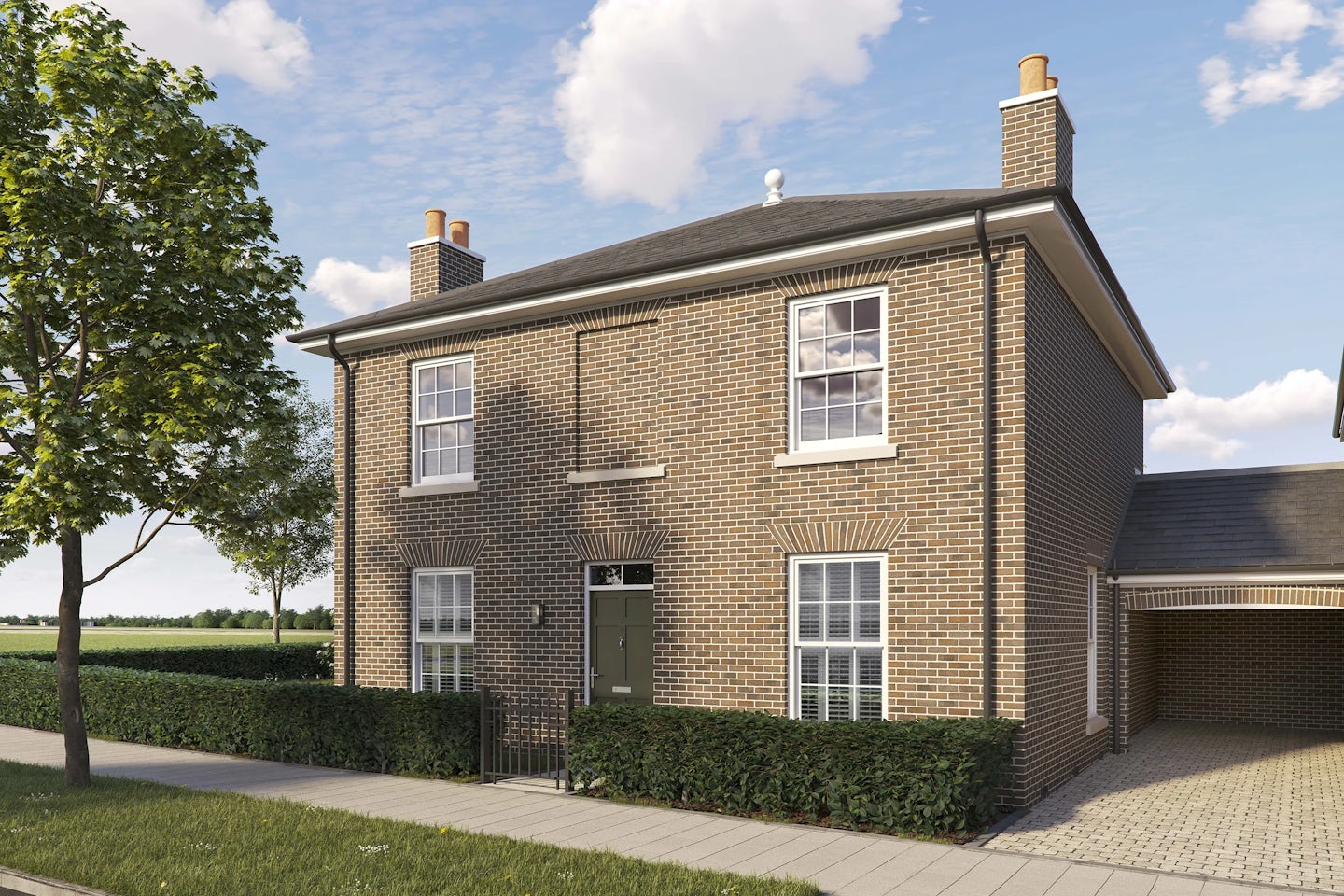 Two-story detached brick house with a pitched roof and white-framed sash windows. The front features a dark green door with a small canopy and two large windows on the ground floor, plus two similar windows above. A low hedge runs along the front of the property, and a paved sidewalk borders the street. A tree is planted on the grass verge to the left, and open fields are visible in the background under a bright blue sky with scattered clouds.