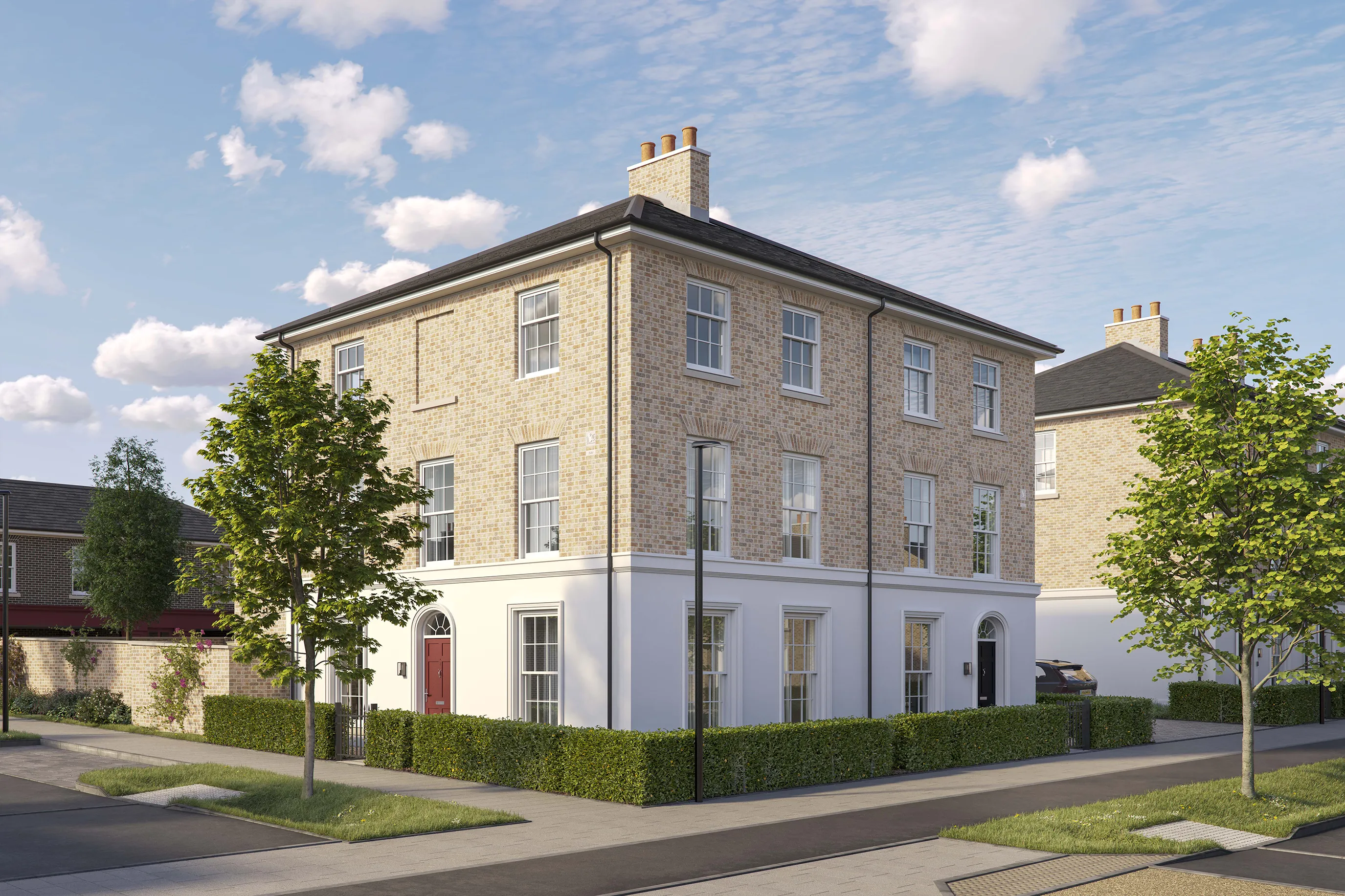 Three-story corner brick townhouse with a pitched roof and white-framed sash windows. The ground floor features a white-painted facade with two front doors, one red and one black, each framed by an arched doorway. Low green hedges border the property, and two young trees are planted along the pavement. The house is situated on a quiet residential street under a bright blue sky with scattered clouds.