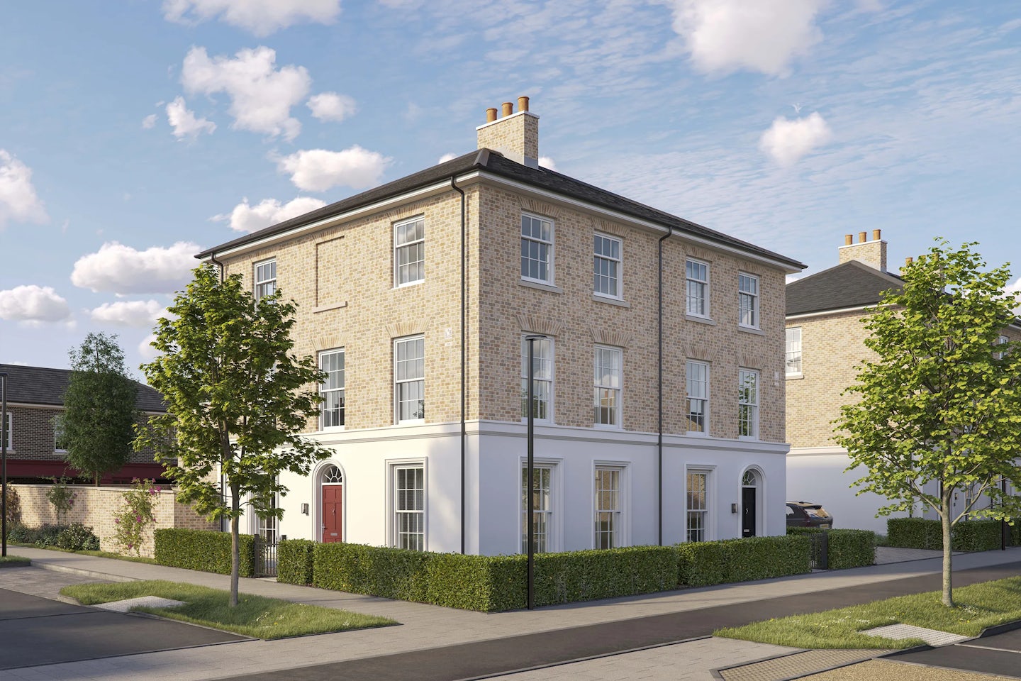 Three-story corner brick townhouse with a pitched roof and white-framed sash windows. The ground floor features a white-painted facade with two front doors, one red and one black, each framed by an arched doorway. Low green hedges border the property, and two young trees are planted along the pavement. The house is situated on a quiet residential street under a bright blue sky with scattered clouds.