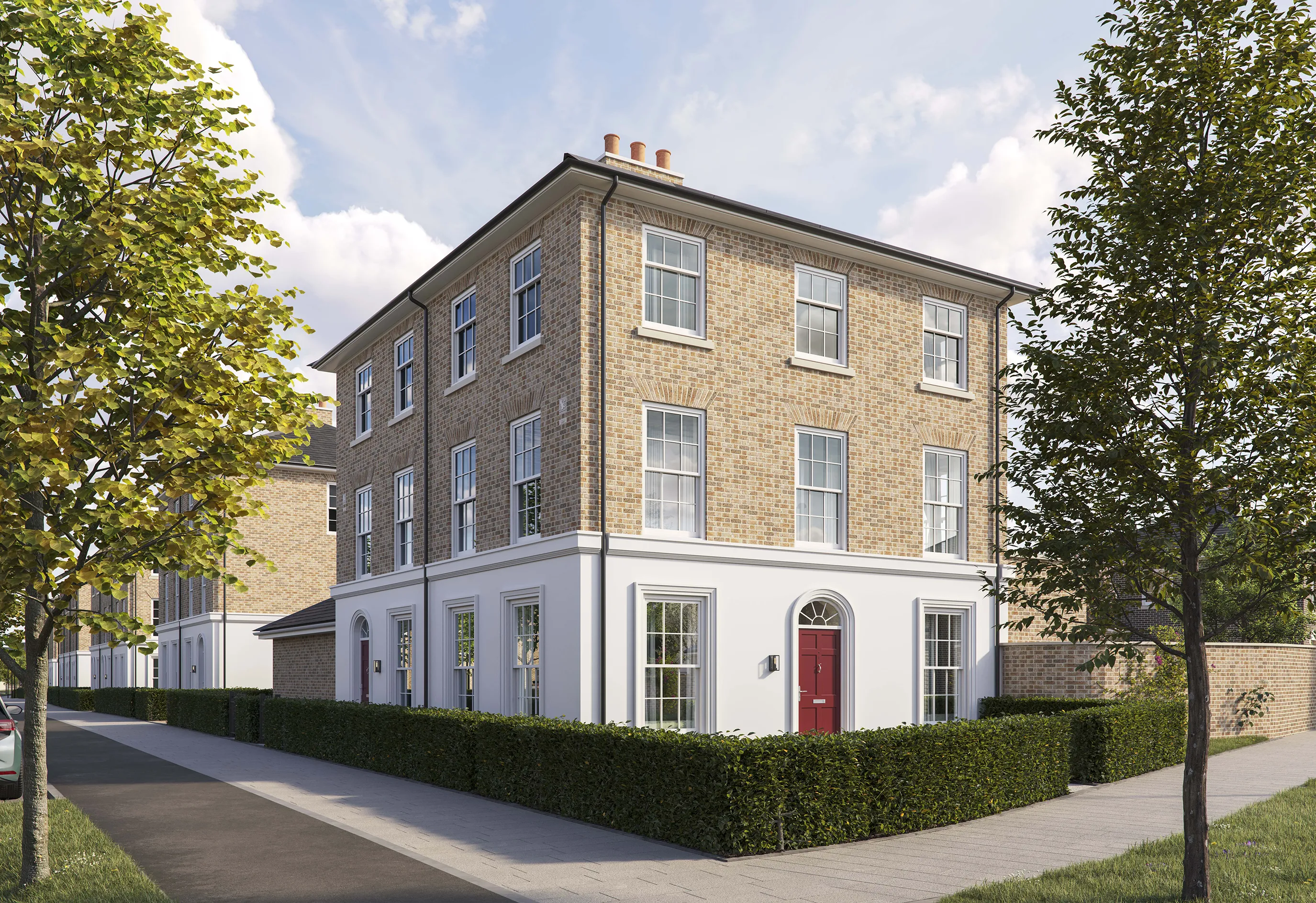 Three-story corner brick townhouse with a pitched roof and white-framed sash windows. The ground floor has a white-painted facade with a central red front door framed by an arched doorway. Low green hedges border the property, and a paved sidewalk runs along the front and side. Two young trees are planted along the pavement, and the sky is bright blue with scattered clouds.