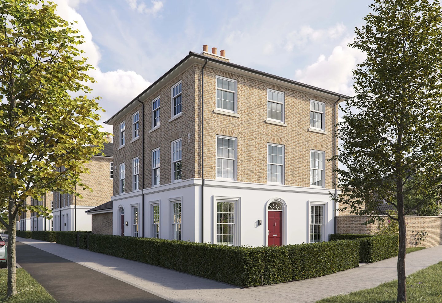 Three-story corner brick townhouse with a pitched roof and white-framed sash windows. The ground floor has a white-painted facade with a central red front door framed by an arched doorway. Low green hedges border the property, and a paved sidewalk runs along the front and side. Two young trees are planted along the pavement, and the sky is bright blue with scattered clouds.