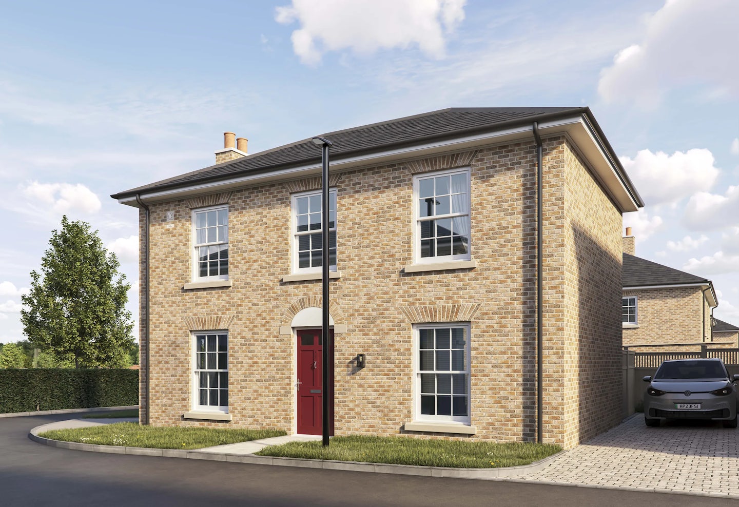 Two-story detached brick house with a pitched roof and white-framed sash windows. The front features a central red door with an arched brick detail above it, flanked by two large windows on the ground floor and two similar windows on the upper floor. A paved driveway with a parked car is visible on the right side, and a curved road runs along the front of the property. The sky is bright blue with scattered clouds.